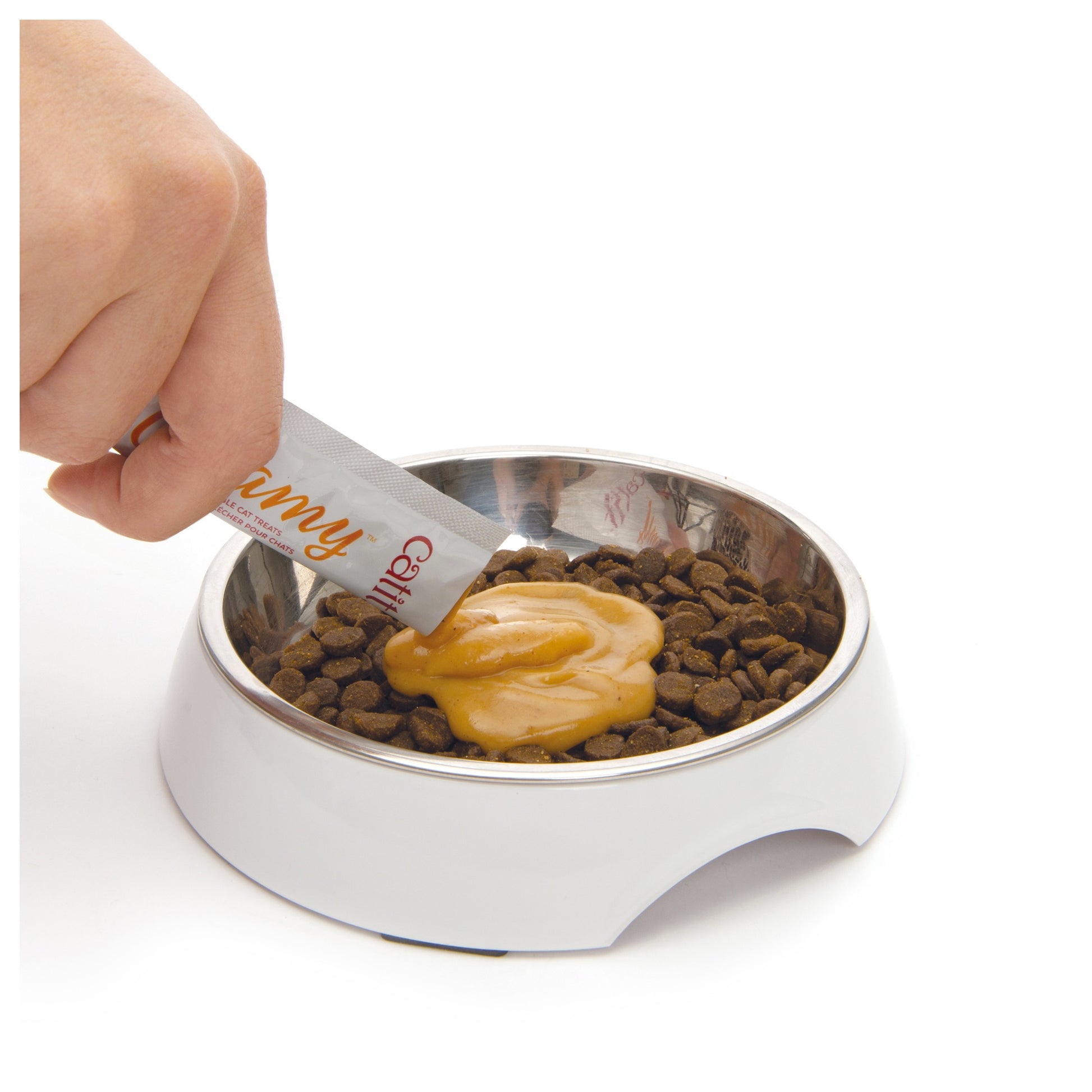 Hand holding a tube of catit creamy over a bowl of cat food with catit on a white background