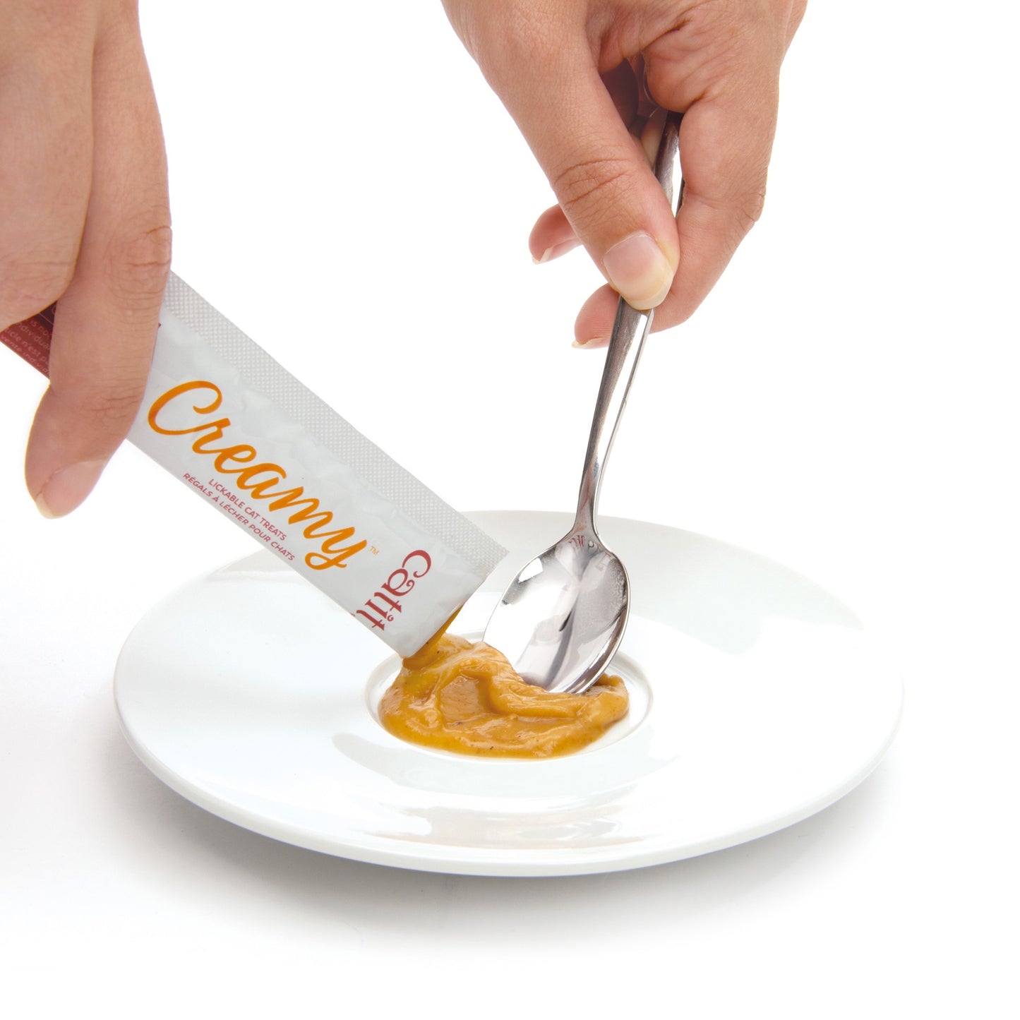 Hand holding a tube labeled 'Creamy' above a spoon with creamy butter on a white plate.