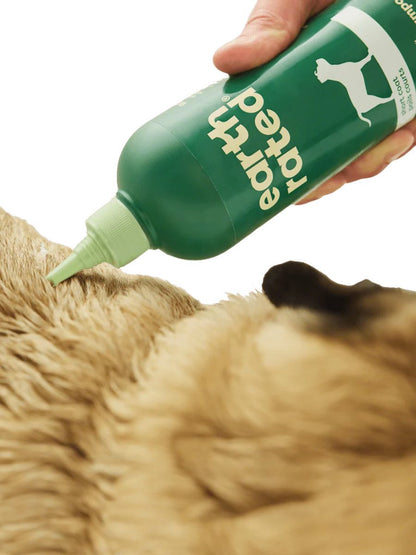 Person applying a green bottle labeled 'Ear Ted' to a dog's ear.